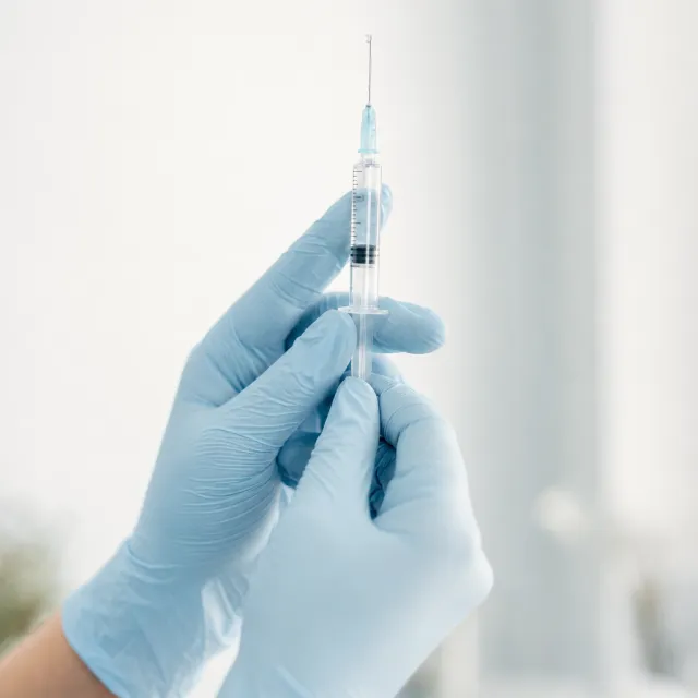 Gloved hands holding a syringe